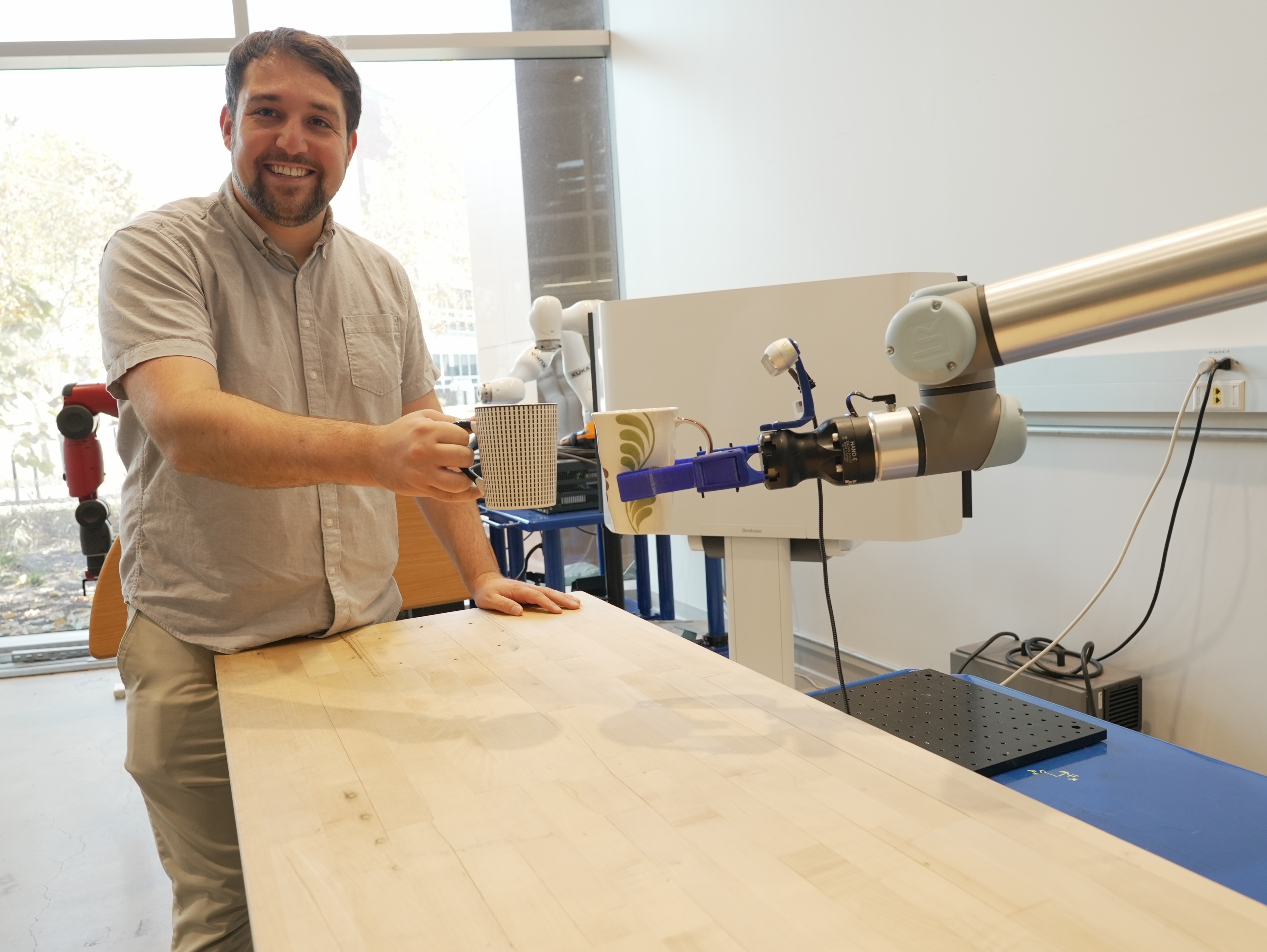 Levi Burner holds a coffee mug next to a robotic arm also gripping a coffee mug.