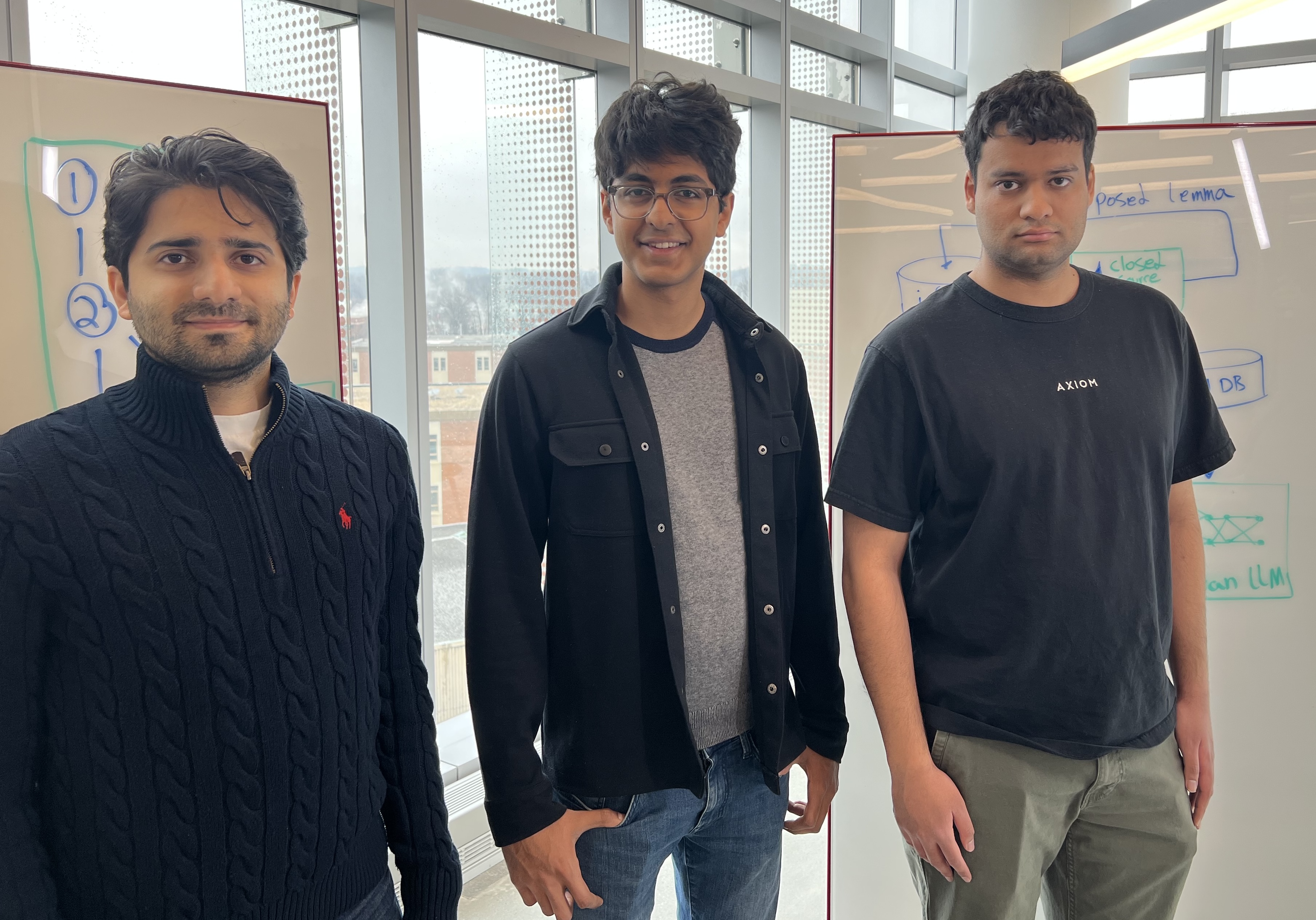 UMD computer science Ph.D. students (from left) Iman Gholami, Arshia Soltani, and Danny Mittal stand in front of white boards covered with diagrams and equations.