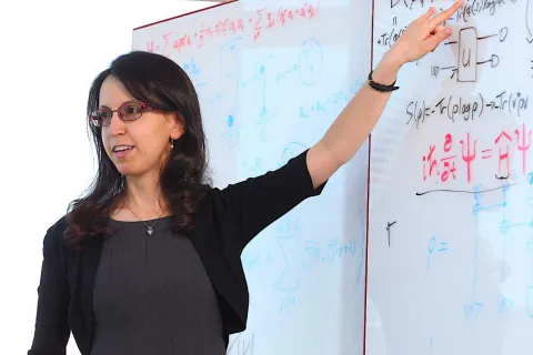 Nicole Yunger Halpern explains complex equations on a whiteboard, pointing to a section with mathematical and quantum notations.