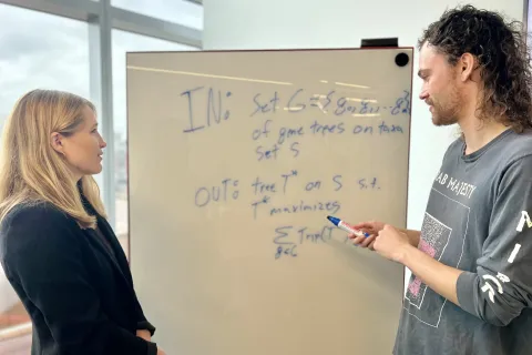 Erin Molloy and a student stand in front of a white board with equations and technical terms written on it. 