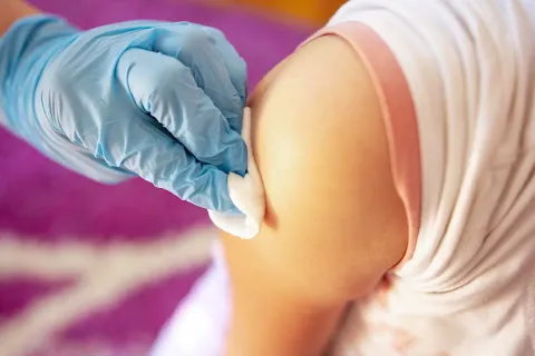 A photo of a nurse swabbing a patient's arm with a cotton ball in preparation for administering a vaccine.