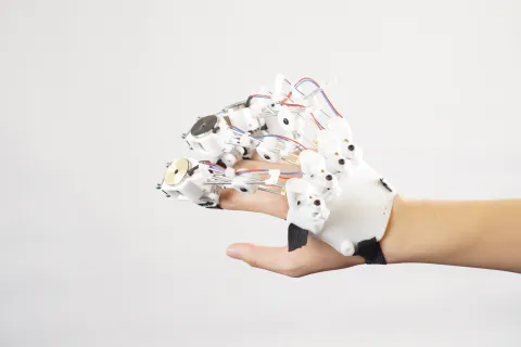 A close-up of a person's hand wearing a complex white robotic exoskeleton glove against a plain white background.