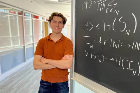 Joseph Carolan leans against a blackboard filled with equations written in white chalk.