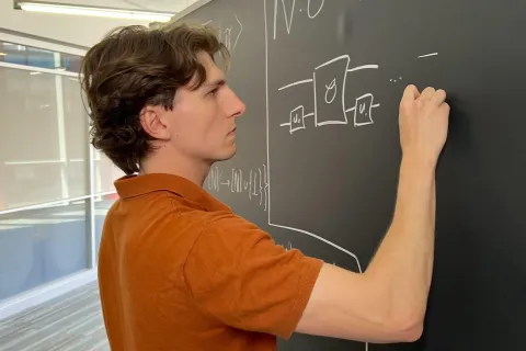 Joseph Carolan writes equations in chalk on a blackboard.