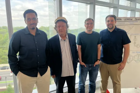 From left to right, Eadom Dessalene, Yiannis Aloimonos, Christopher Metzler, and Levi Burner stand together by a large window for a group photo.