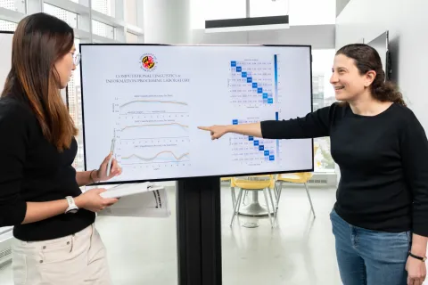 Naomi Feldman, right, points to data charts on a digital display while discussing them with a colleague.