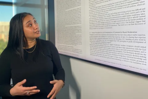 Lovely-Frances Domingo discusses a study on AI and Reddit moderation, projected onto a screen beside her.