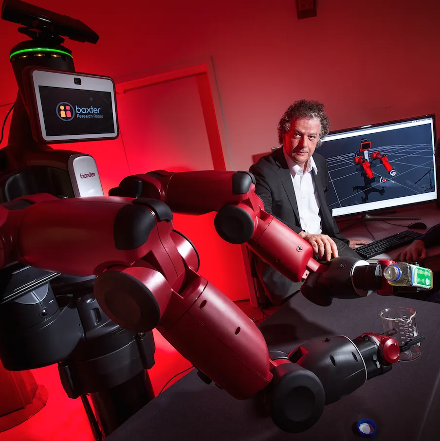 Yiannis Aloimonos sits with a Baxter Research Robot next to him.
