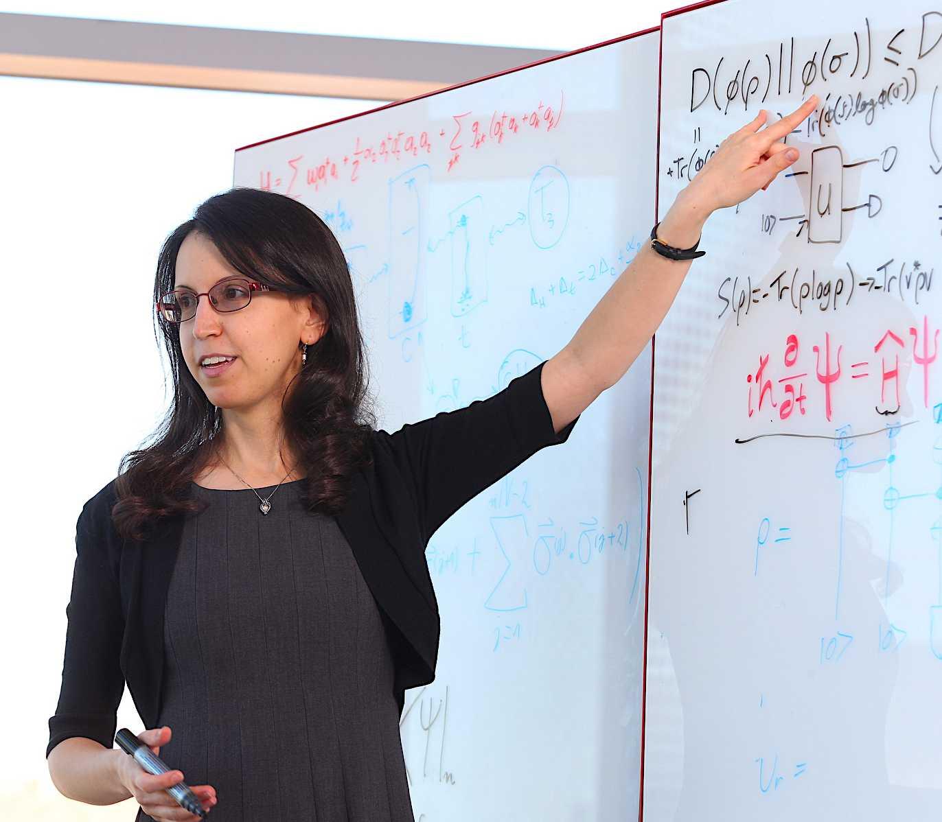 Nicole Yunger Halpern explains complex equations on a whiteboard, pointing to a section with mathematical and quantum notations.