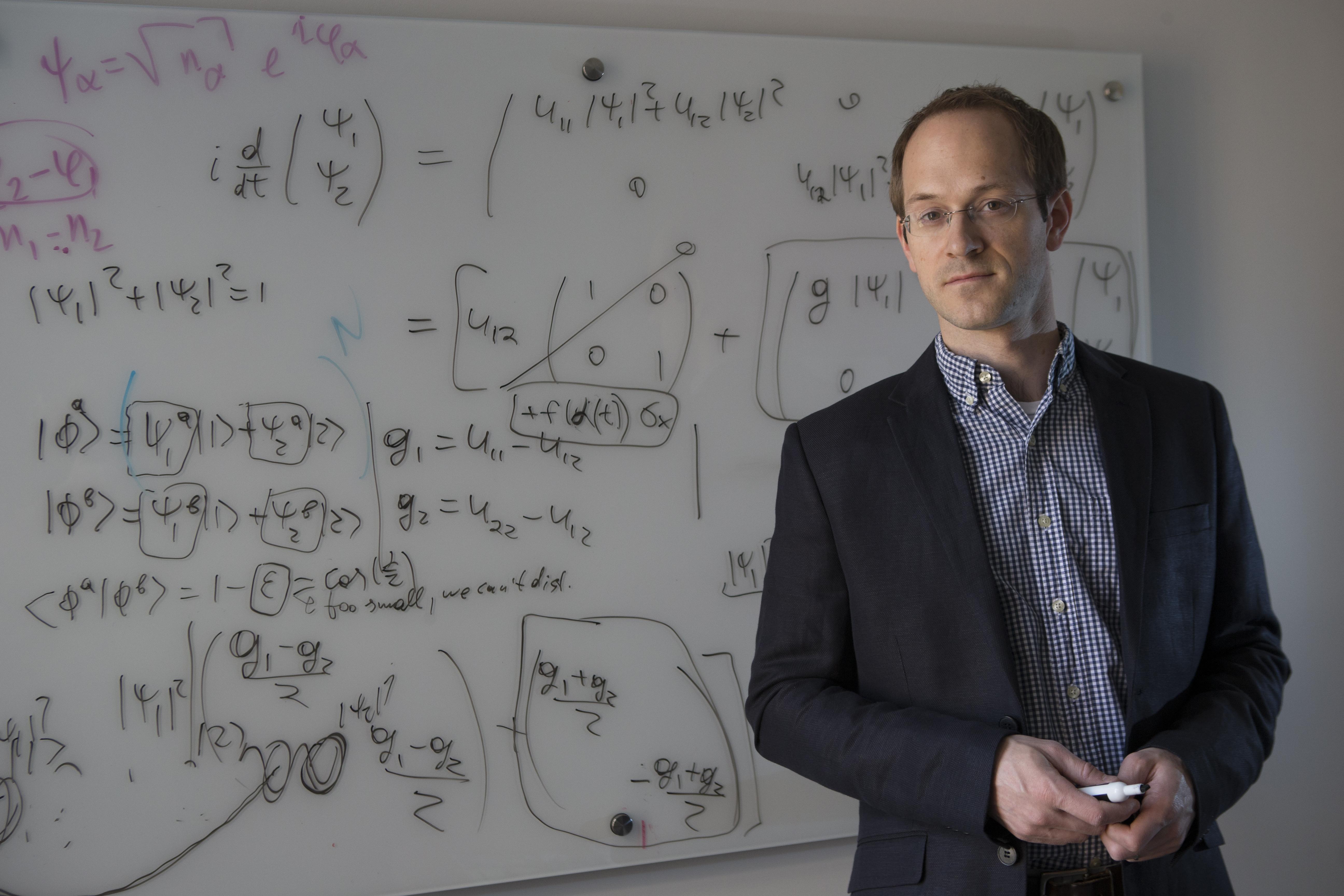 A photo of Andrew Childs in front of a white board with numerous equations written on it.