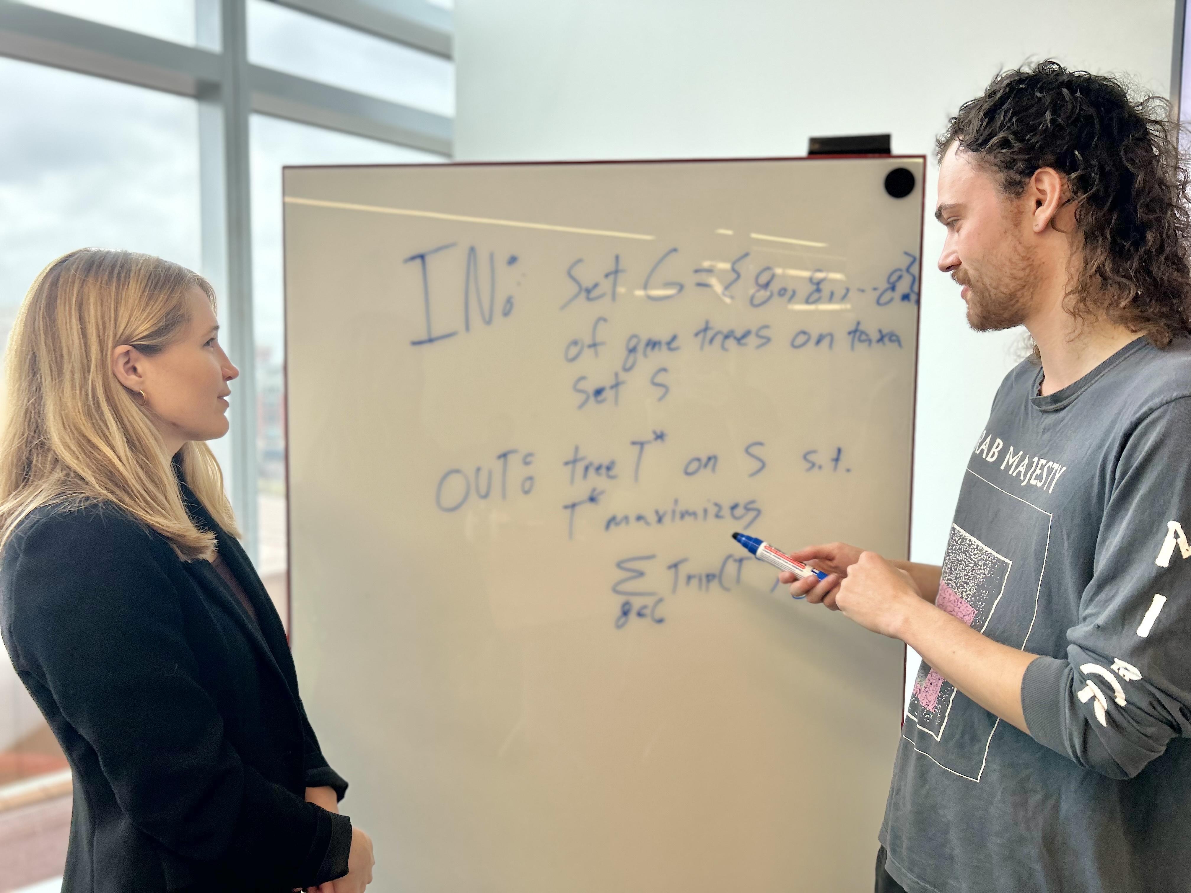 Erin Molloy and a student stand in front of a white board with equations and technical terms written on it. 
