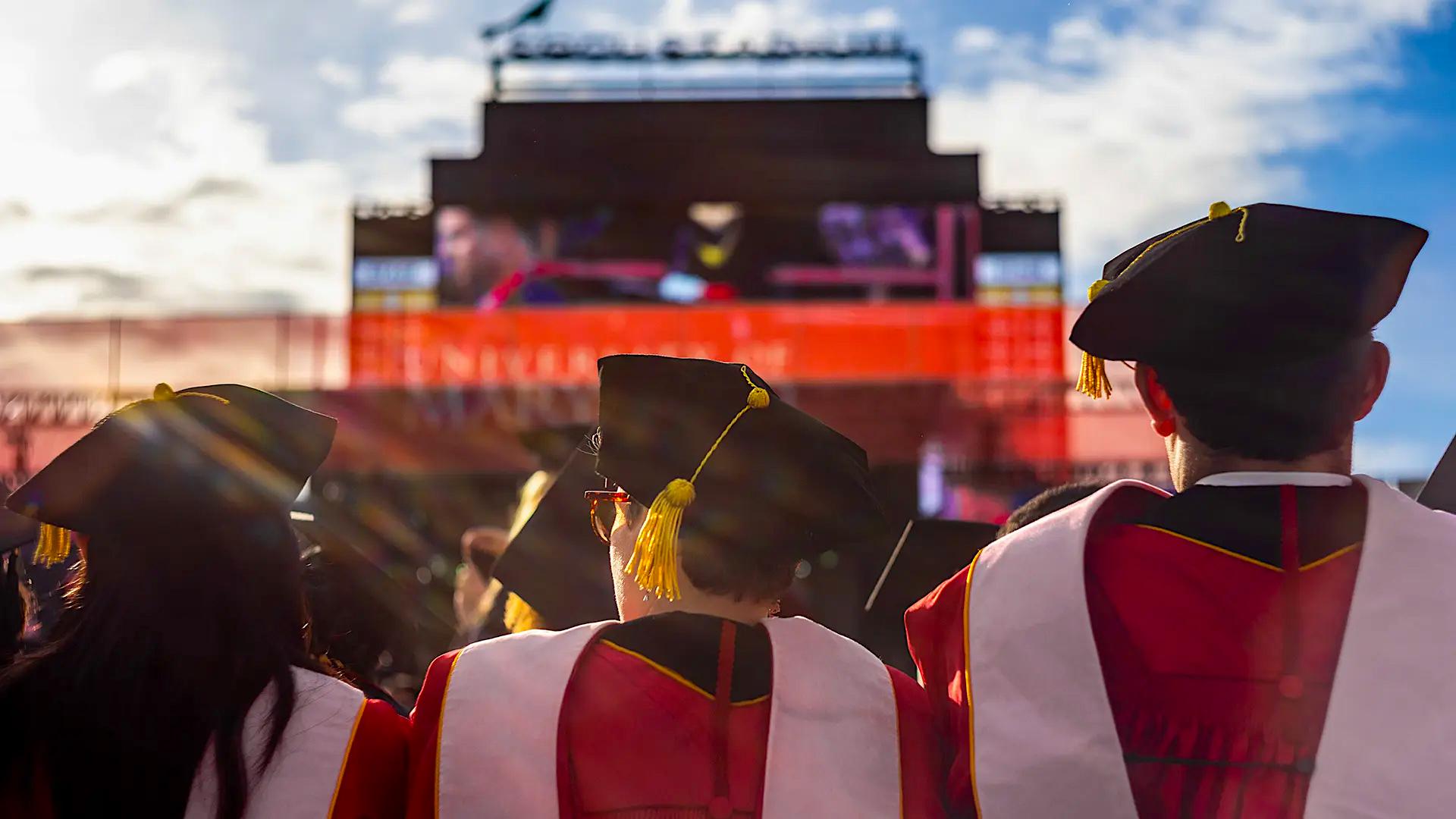 Three students in graduation gowns and caps facing away from camera