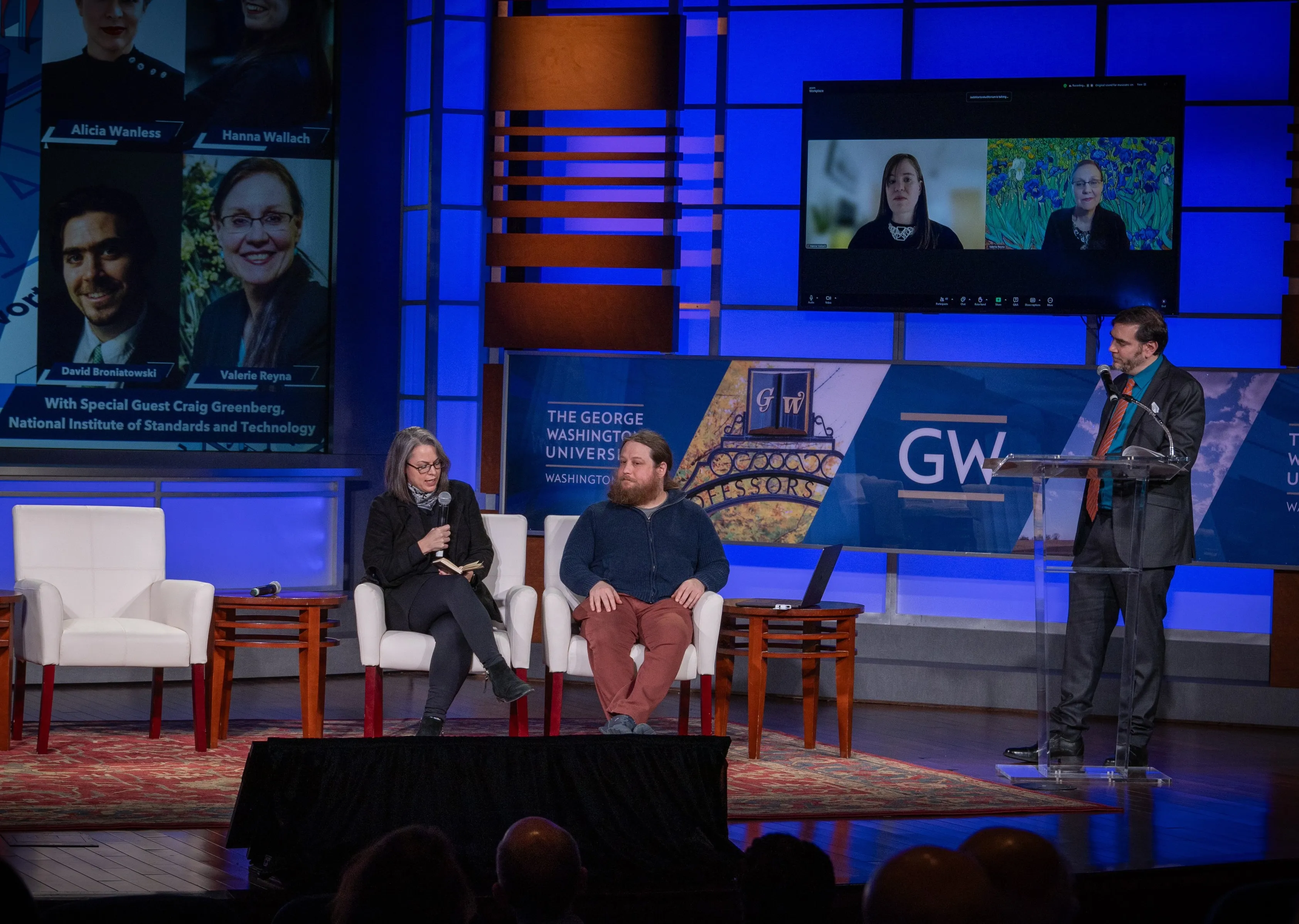 stage of a conference with 2 guest speakers sitting on sofas and the anchor