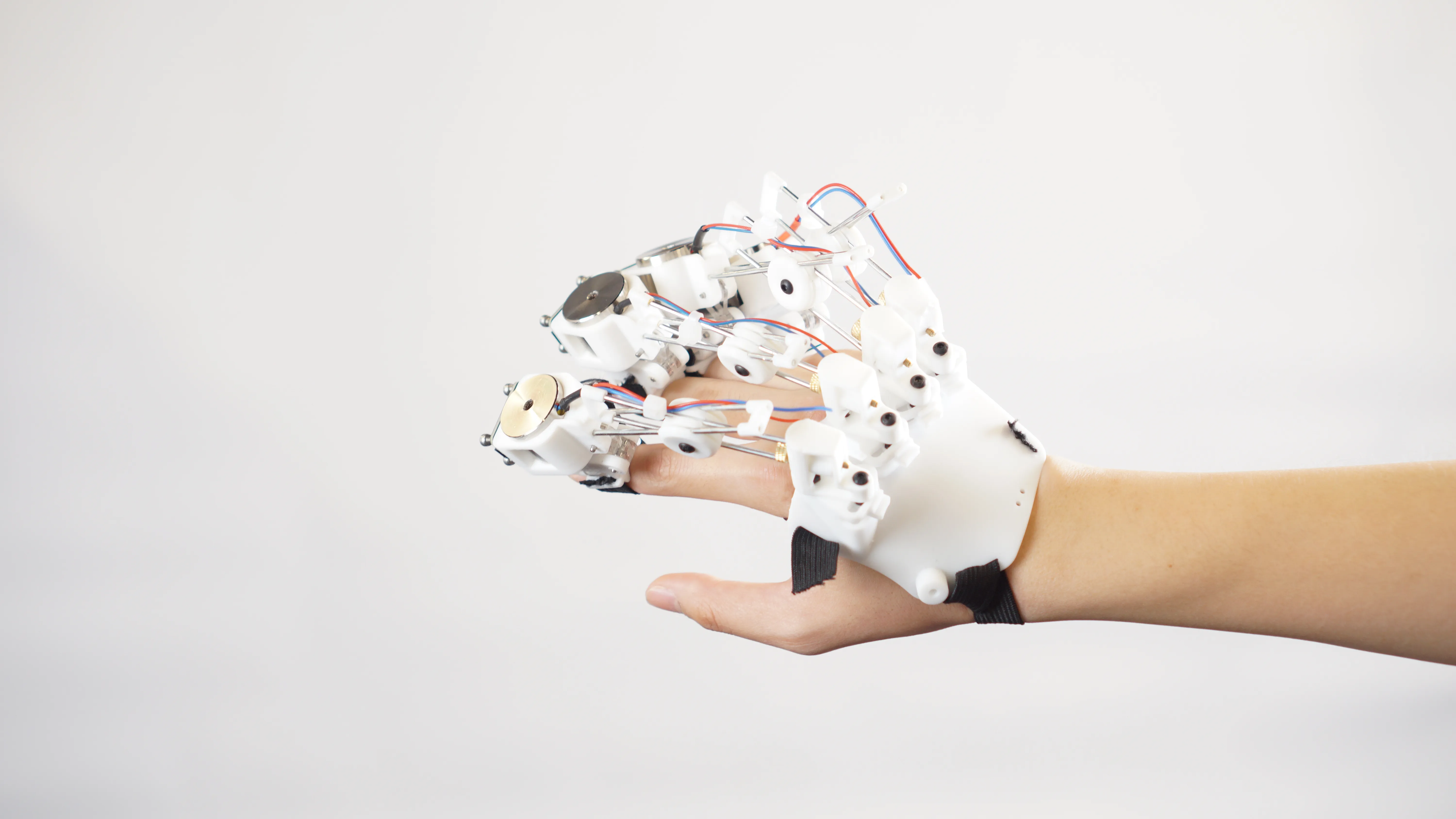 A close-up of a person's hand wearing a complex white robotic exoskeleton glove against a plain white background.