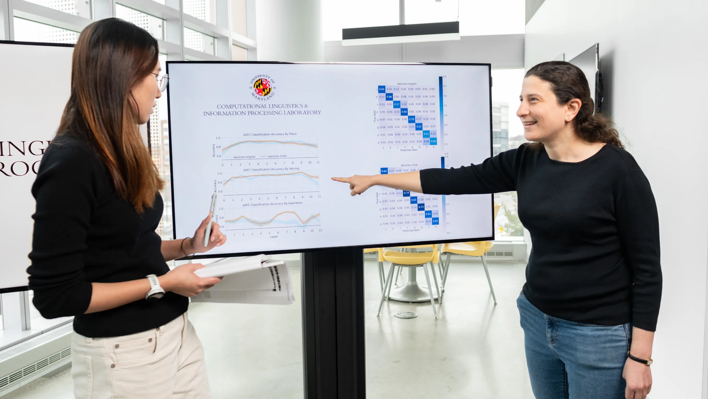 Naomi Feldman, right, points to data charts on a digital display while discussing them with a colleague.
