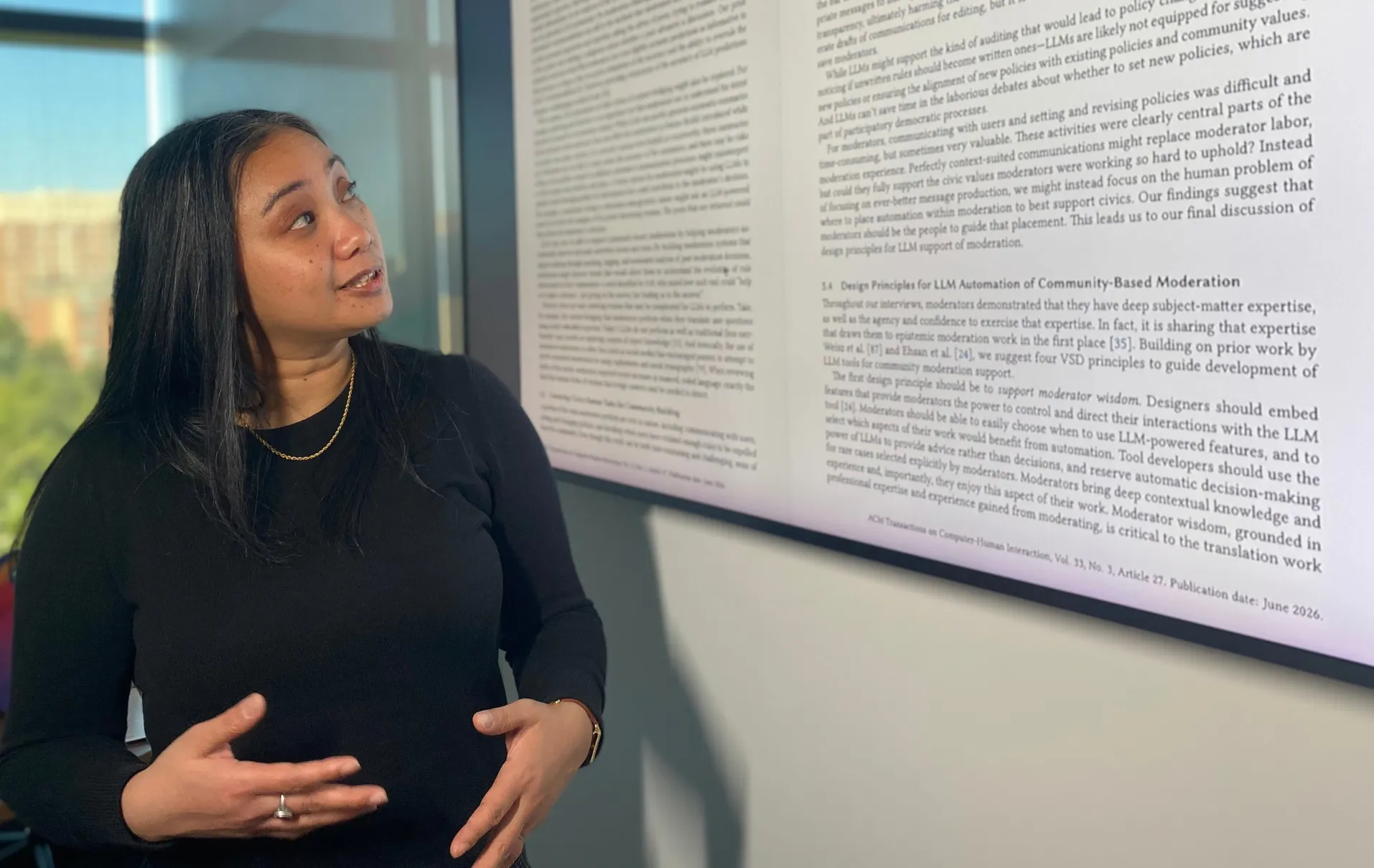 Lovely-Frances Domingo discusses a study on AI and Reddit moderation, projected onto a screen beside her.